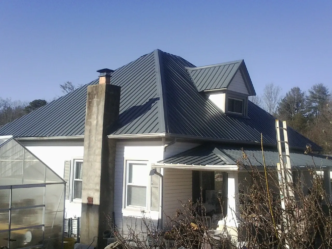 Dark blue standing seam metal roof on a white farmhouse with dormer — Slate & Tile Roof Repair by Roofing Brothers in Ferguson
