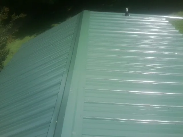 New green metal panels meeting at the ridge of a roof — Flat Roof Repair work by our crew in Ferguson