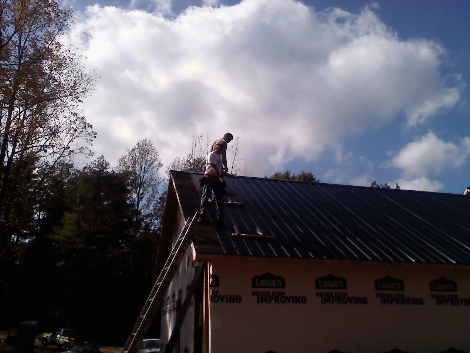 Roofer fastening dark metal panels high against a cloudy sky, from a Roof Inspection job in Ferguson