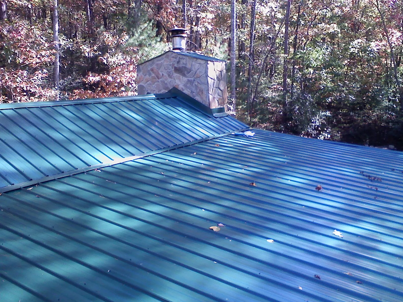 New green metal roof and stone chimney surrounded by autumn woods in Ferguson