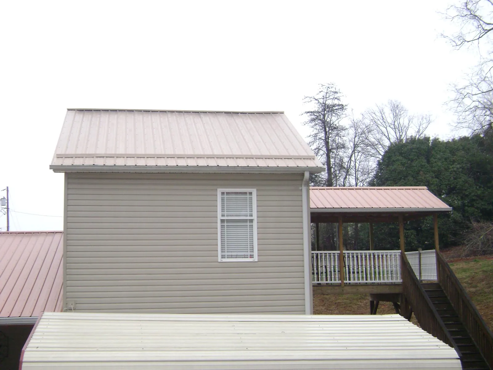 Tan metal roofs on a two story addition and attached porch, from a Roof Replacement job in Ferguson